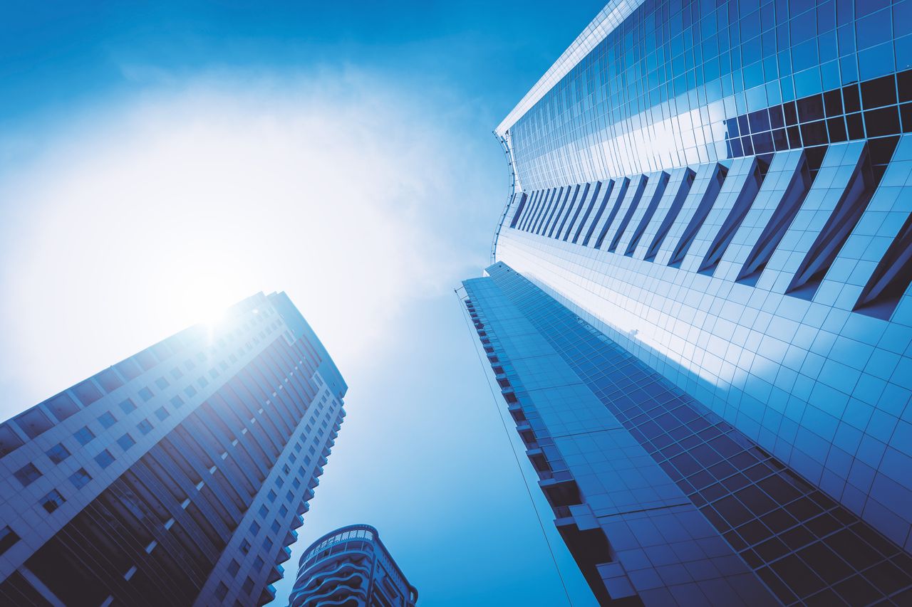 Low angle view of futuristic skyscrapers in a cityscape against a bright blue sky