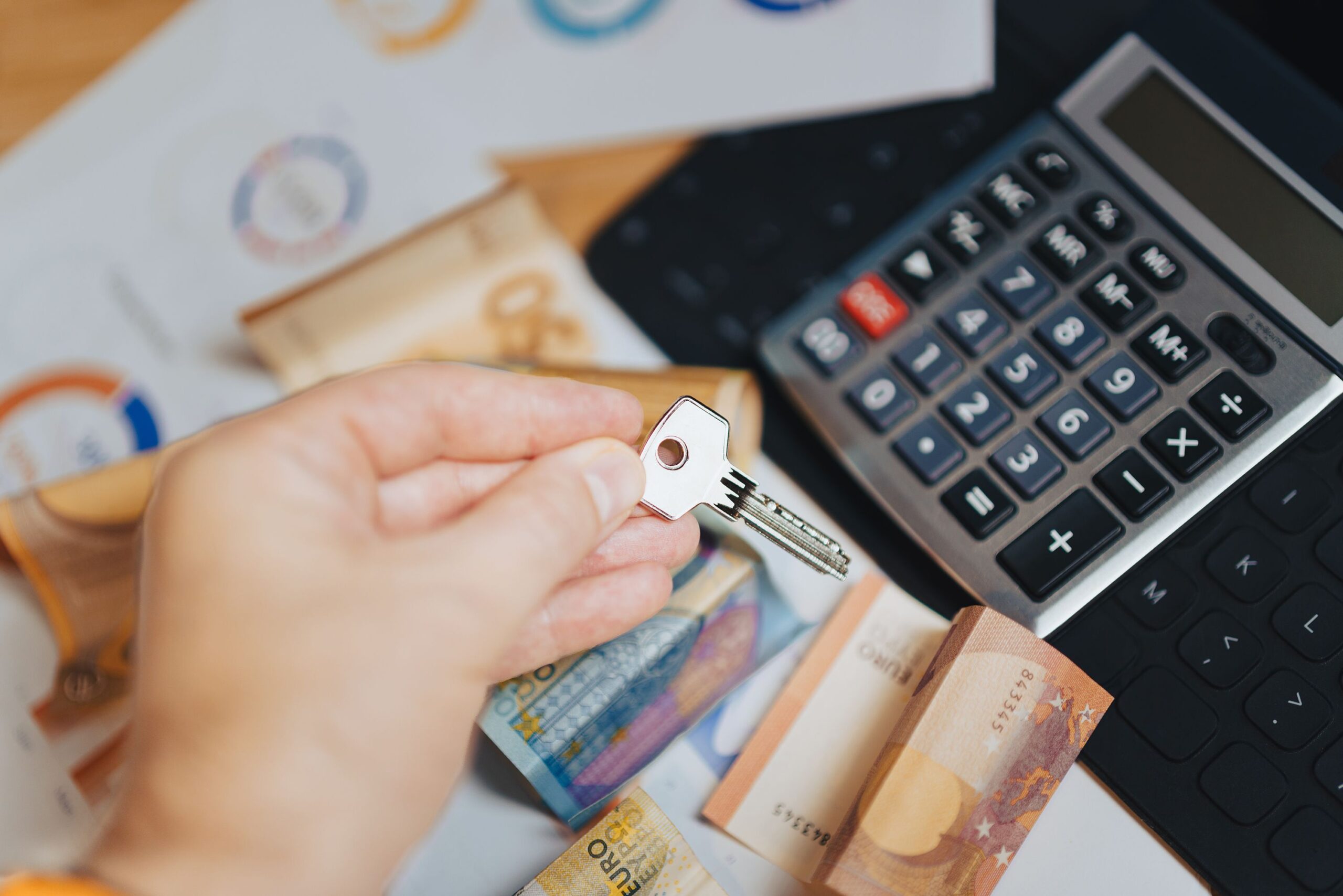 Hand holding key above Euro banknotes and calculator, symbolizing real estate investment