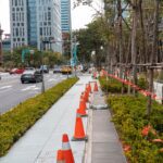 Perspective of an urban street lined with traffic cones, plants, and high-rise buildings