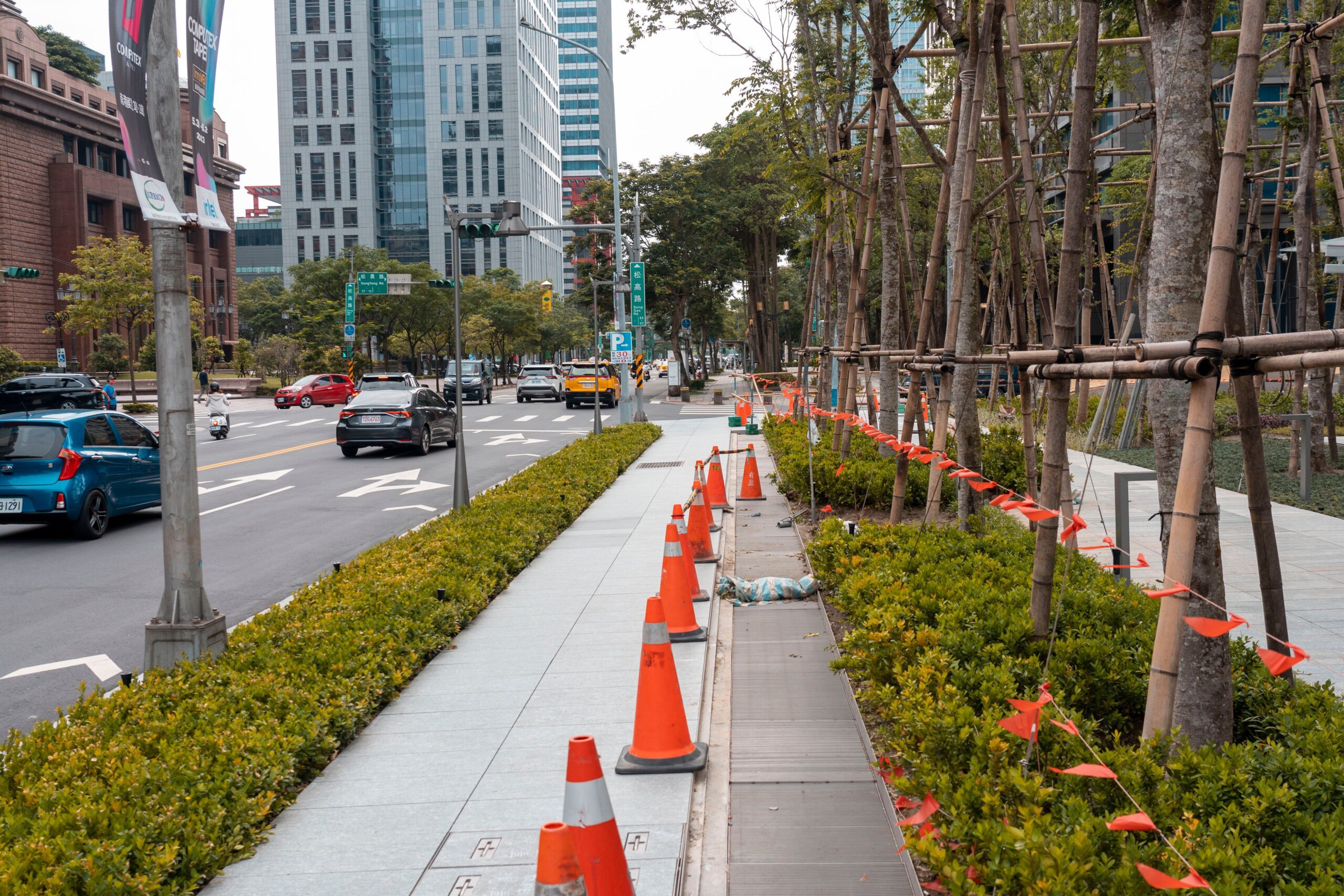 Perspective of an urban street lined with traffic cones, plants, and high-rise buildings